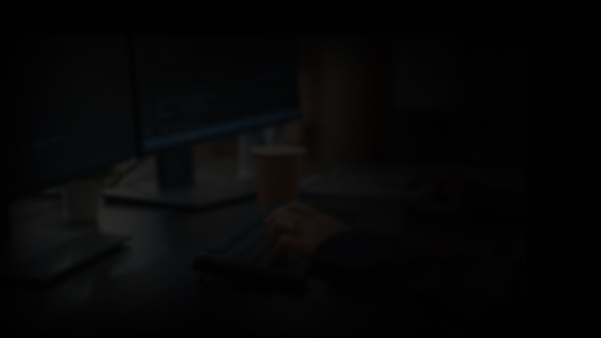 Hände tippen Programmcode auf einer Tastatur vor mehreren Bildschirmen
