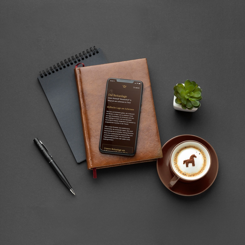 Schreibtisch von oben mit Notizbüchern, Stift, Kaffee und Smartphone mit geöffneter Website